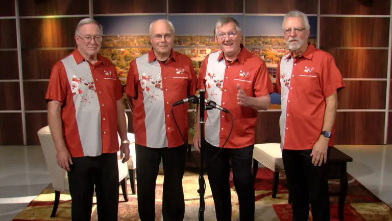 Four men in Christmas themed bowling shirts prepare to sing.