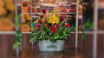 A floral arrangement sits on a table with the word "Garden" on the tin pot.