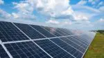 An array of solar panels in a field with blue skies and fluffy white clouds.