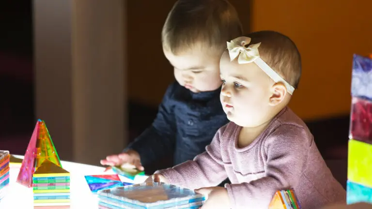 Two children play at a light up table with multicolored plastic shapes.