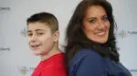 A young boy in a red t-shirt stands with his back to a woman in a blue shirt. They are in front of a background that says turning pointe autism foundation.