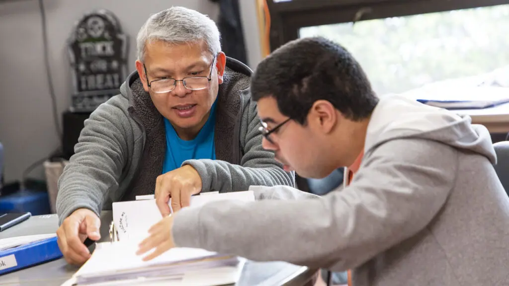 An older gentleman helps a young man, a client of Ray Graham Association, with paperwork.