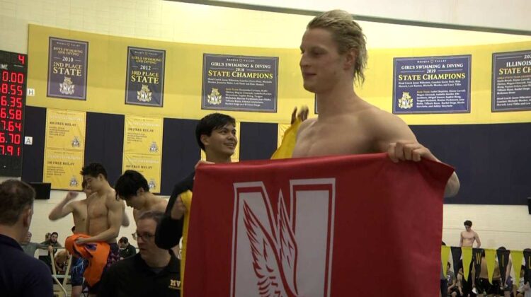 Naperville area swimmers compete in 2024 Olympic Swimming Trials. Alex Lakin holds up Naperville Central flag.
