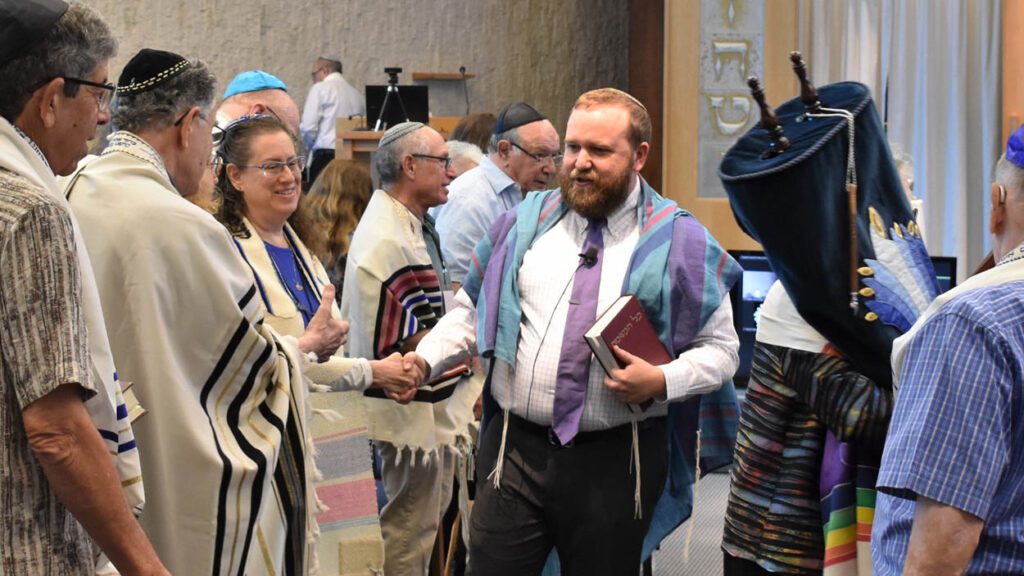 Rabbi David Eber shakes hands surrounded by a group of people.