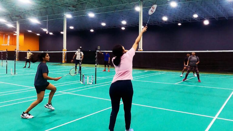 A girl in a pink shirt reached up with a badminton racquet to hit the shuttle.