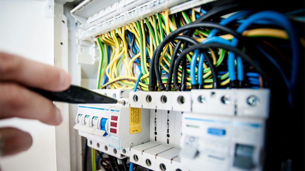 A hand works on an open electrical circuit board.