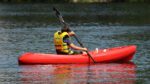 A young boy in a yellow life jackets rows a canoe on the water