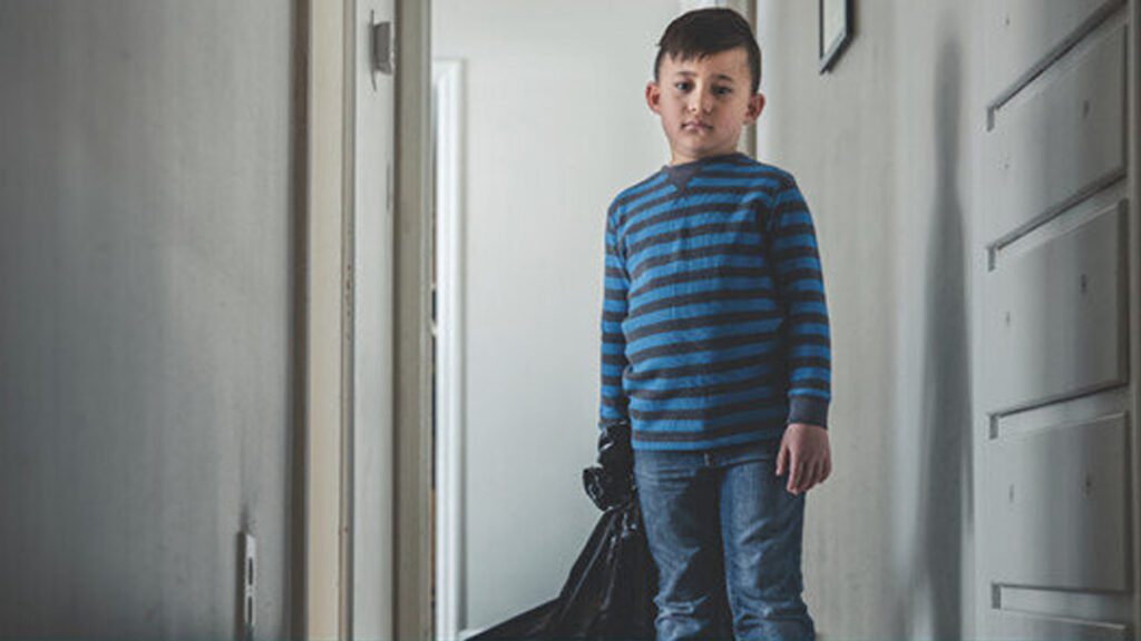 A child stands with his belongings in a garbage bag.