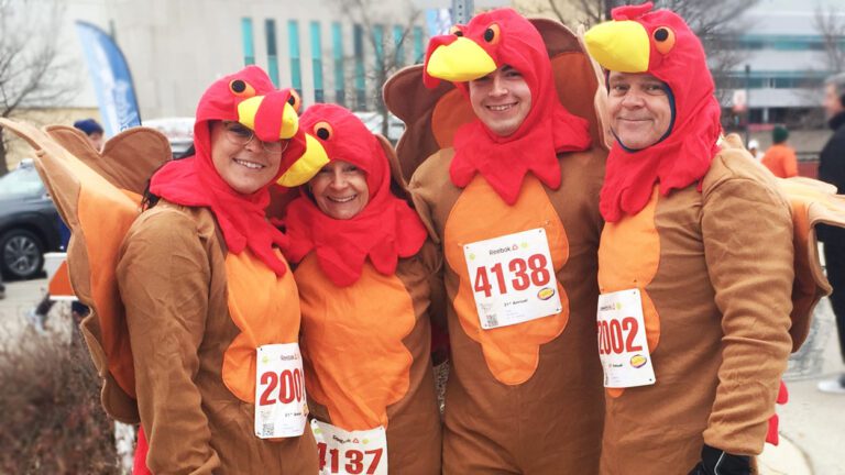 Four people dressed in Turkey onesies with race bibs on for the Naperville Turkey Trot