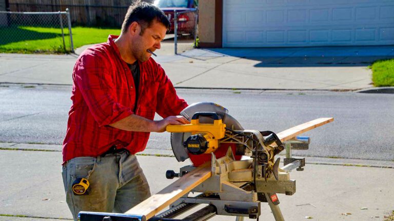 A man working outside uses a saw to cut wood.