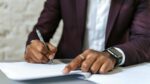 Close up of a man's hands that are signing a document.