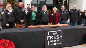 officials stand behind table with giant baguette at The Fresh Market opening