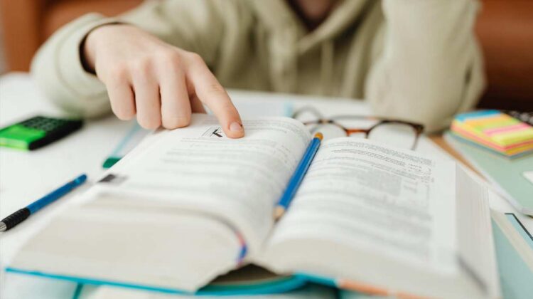 Student looking at book with finger on page