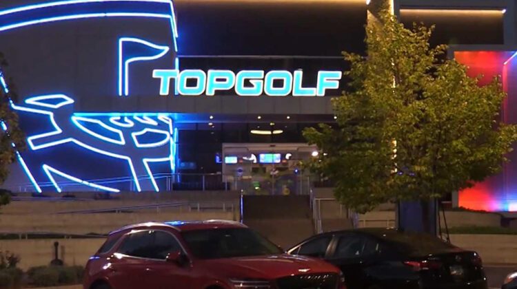 The Top golf sign in lit at night with a red car in the parking lot of the building.